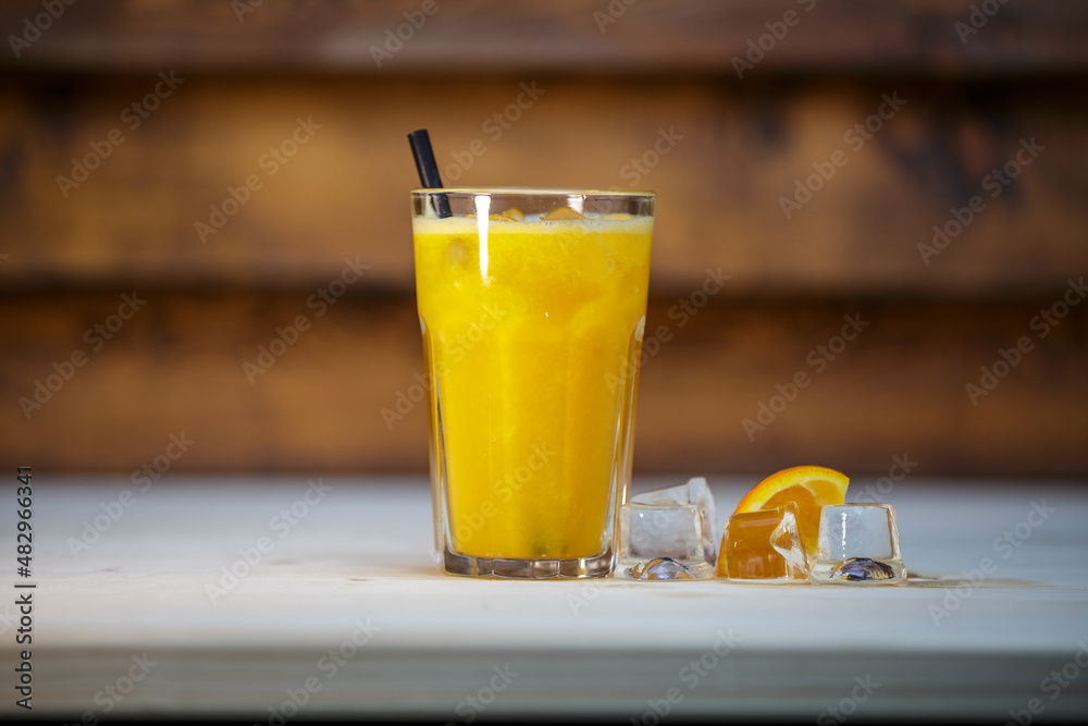 Fresh orange juice with crushed ice and straw on table with wood background