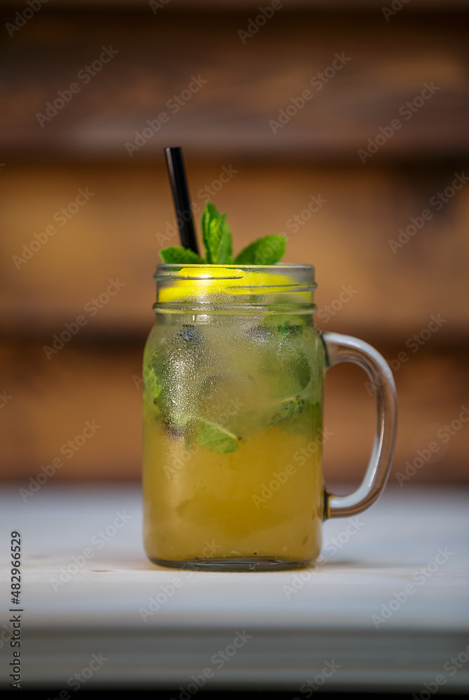 Fresh lemon and mint lemonade with crushed ice and lime and straw on table with wood background