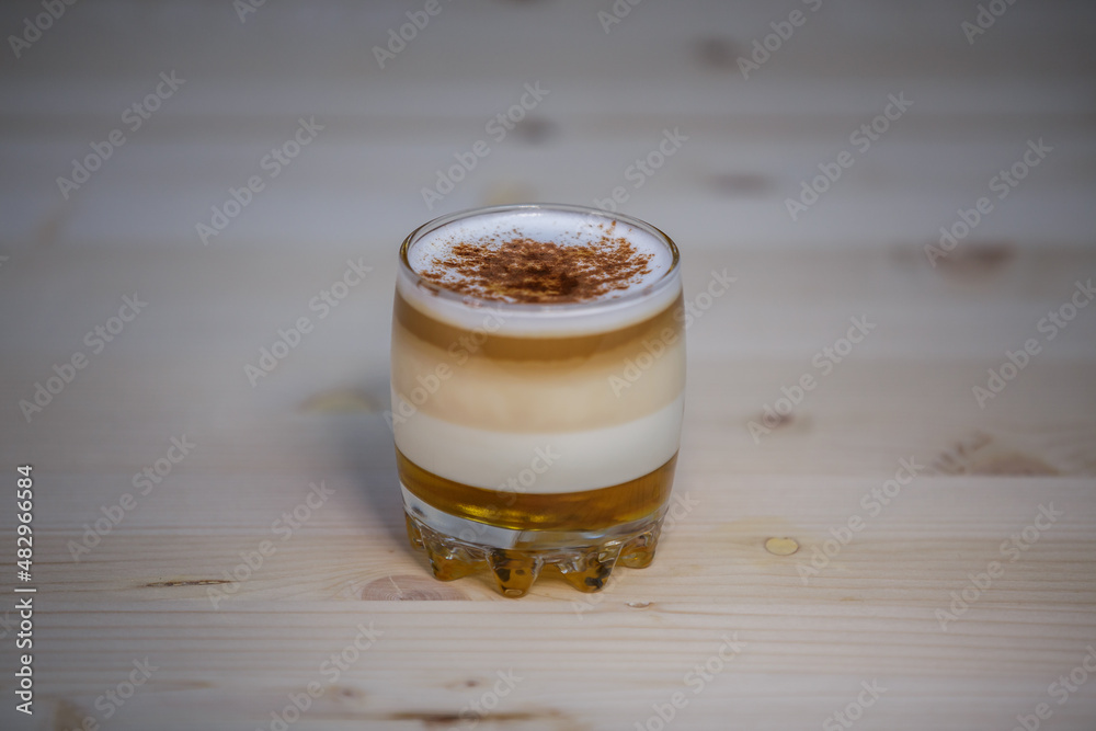 Layered coffee with cinamon in short glass from angle on table with wood background