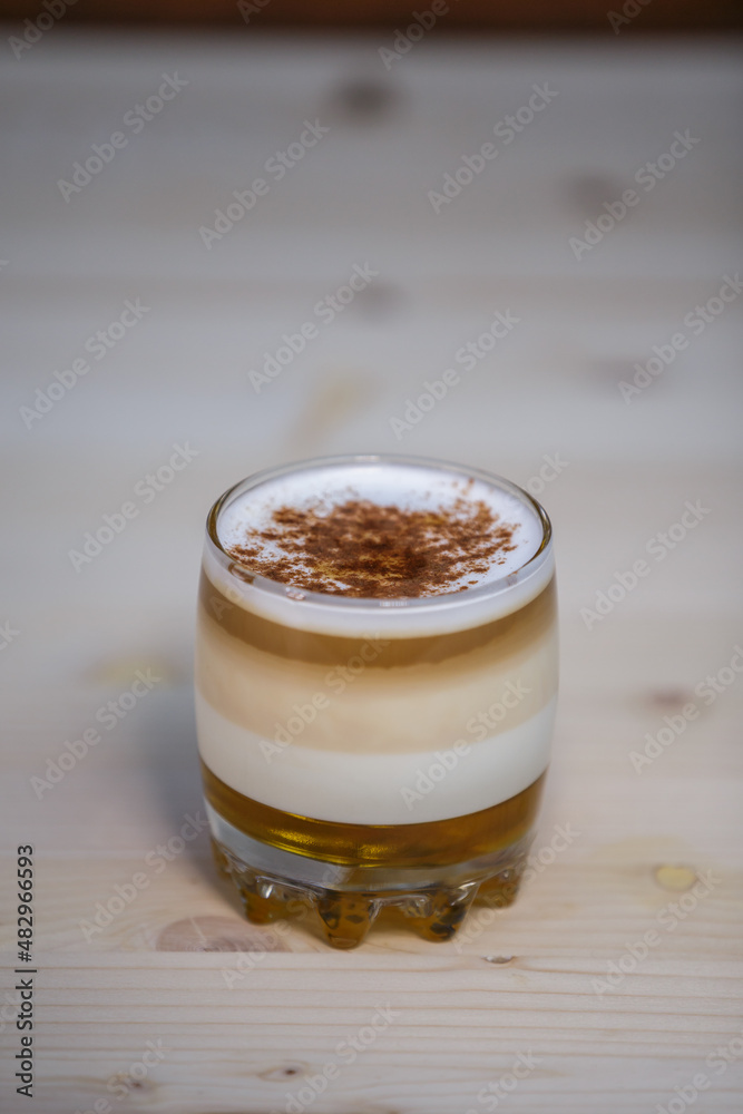 Layered coffee with cinamon in short glass from angle on table with wood background