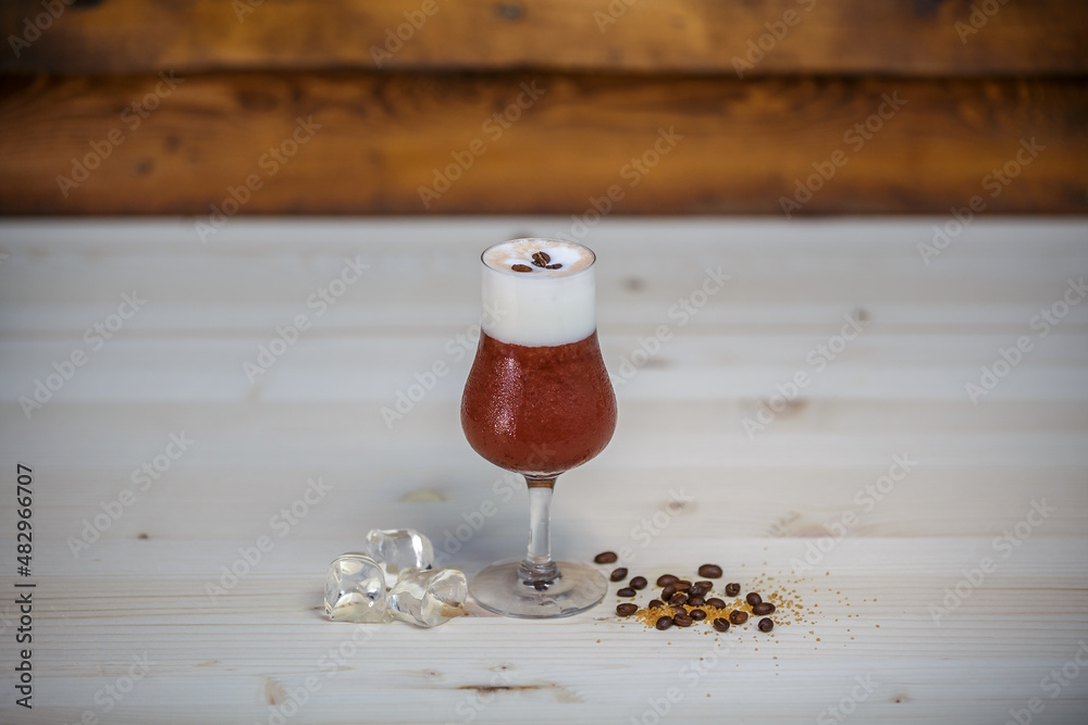 Crushed ice coffee with cinamon in brandy glass from angle on table with wood background and coffee 