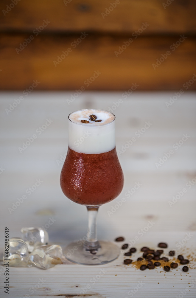 Crushed ice coffee with cinamon in brandy glass from angle on table with wood background and coffee 