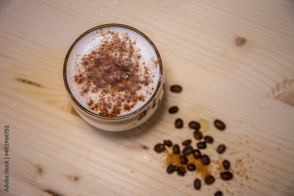 Layered coffee with cinamon in short glass from above on table with wood background and coffee beans