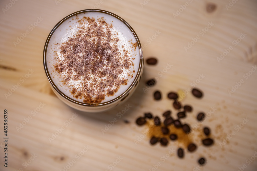 Layered coffee with cinamon in short glass from above on table with wood background and coffee beans