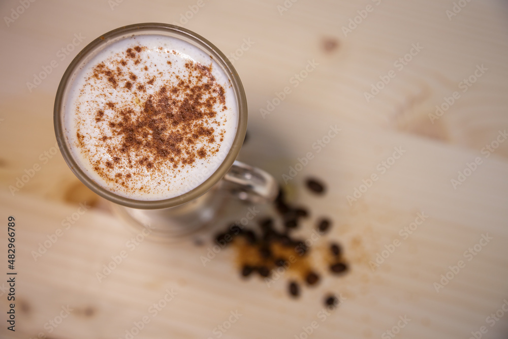 Cappucino with cinamon in tall glass from above on table with wood background and coffee beans