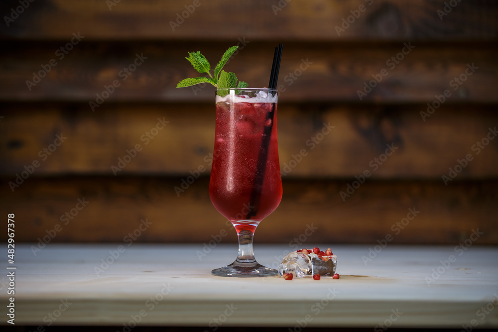 Fresh cold pomegranate cocktail with mint and crushed ice on table with wood background