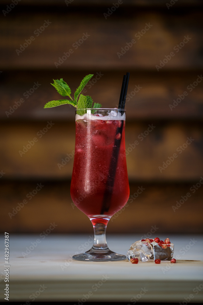 Fresh cold pomegranate cocktail with mint and crushed ice on table with wood background