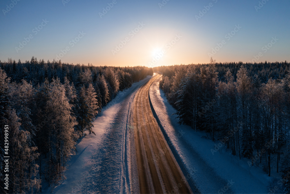 穿过白雪皑皑的北方森林走向日落的道路。芬兰的交通和景观