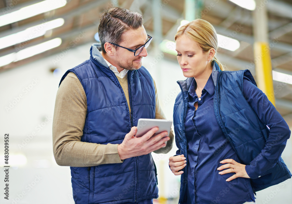 We need this order tracked. Shot of two people using a digital tablet while working in a warehouse.