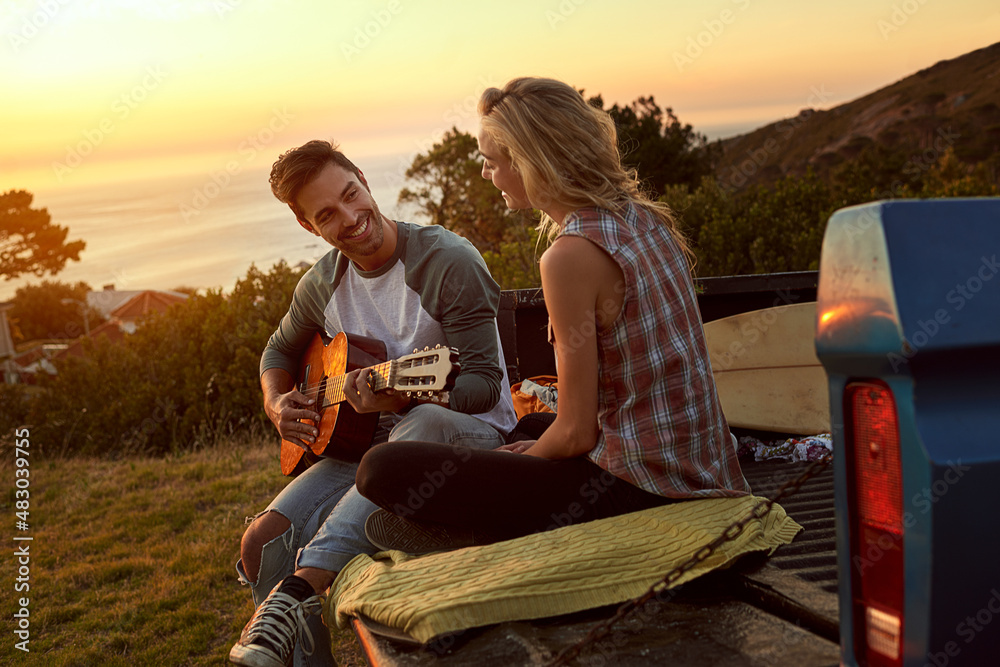 Songs from the heart. Shot of a young man playing guitar for his girlfriend on a roadtrip.