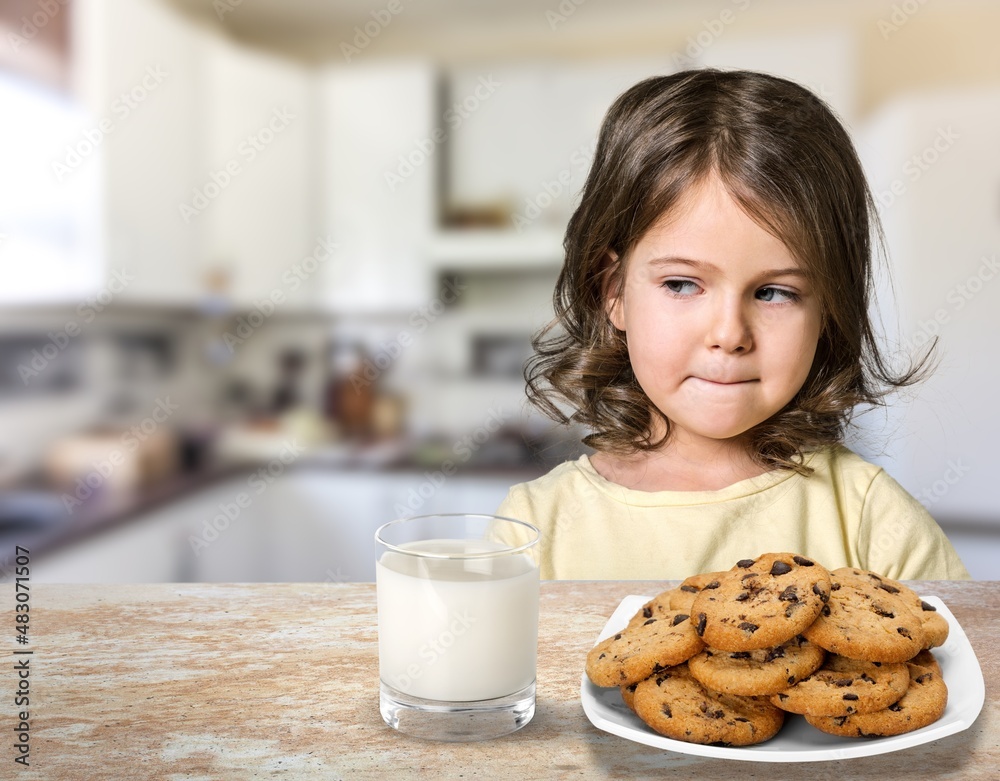 Portrait of sad girl holding glass of milk and dreaming, sitting on dinning table in kitchen interio