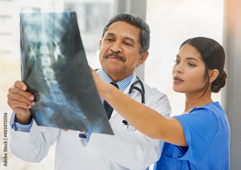 Seeing right through to the problem. Shot of a mature doctor and young nurse looking at an x ray tog