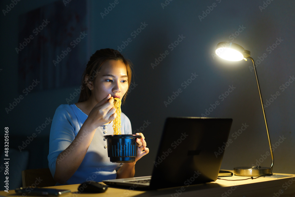 Asian freelancer smart business woman eating instant noodles while working on a laptop in the living