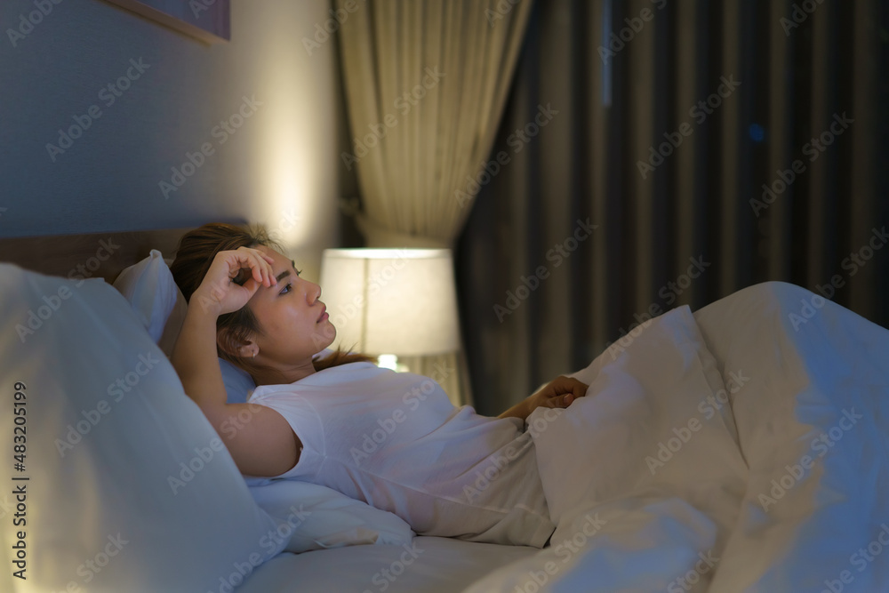 Asian woman lying on a white bed in the bedroom looking worried or thinking about something about he