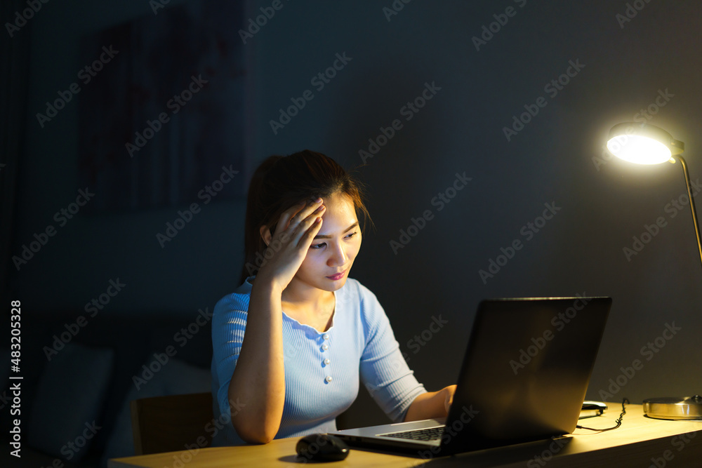 Asian woman work late at night stressful with project research problems on a laptop computer or note