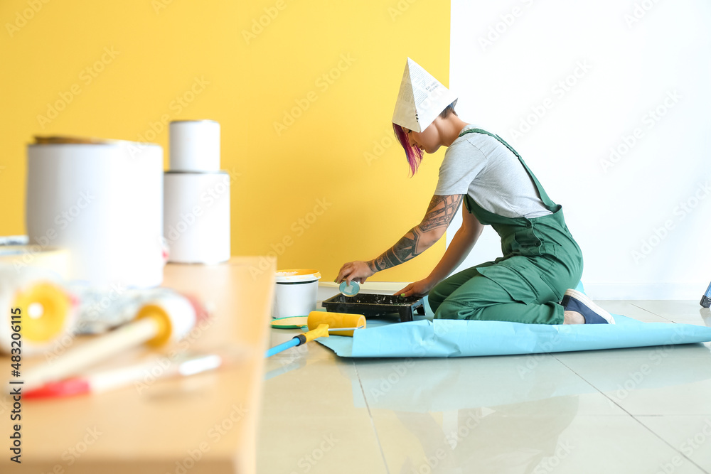 Female decorator pouring paint into tray near color wall