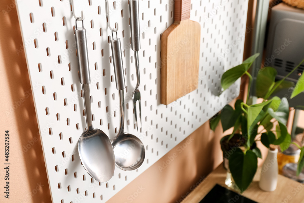 Pegboard with kitchen utensils near color wall, closeup