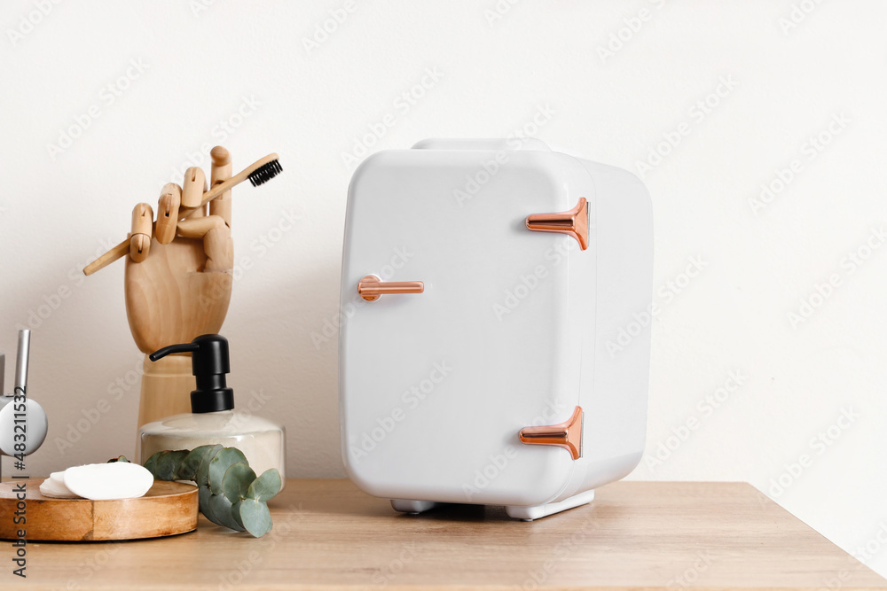 Small cosmetic refrigerator, wooden hand and bath supplies on table near light wall