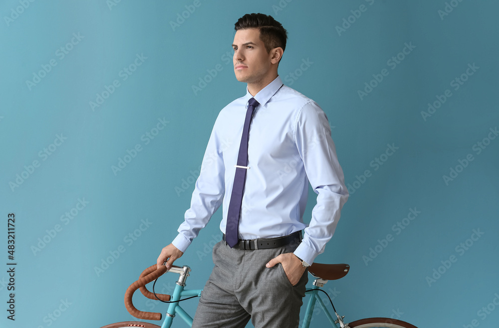 Handsome man in formal clothes with bicycle on color background