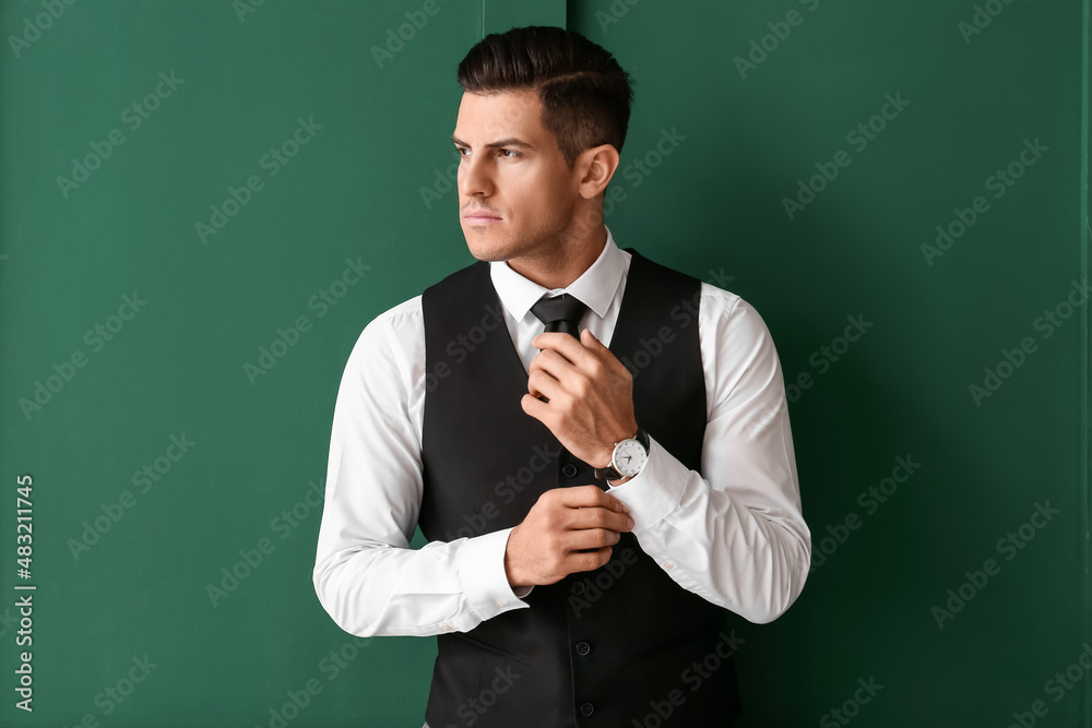 Gentleman in stylish clothes looking aside and adjusting sleeve on color background