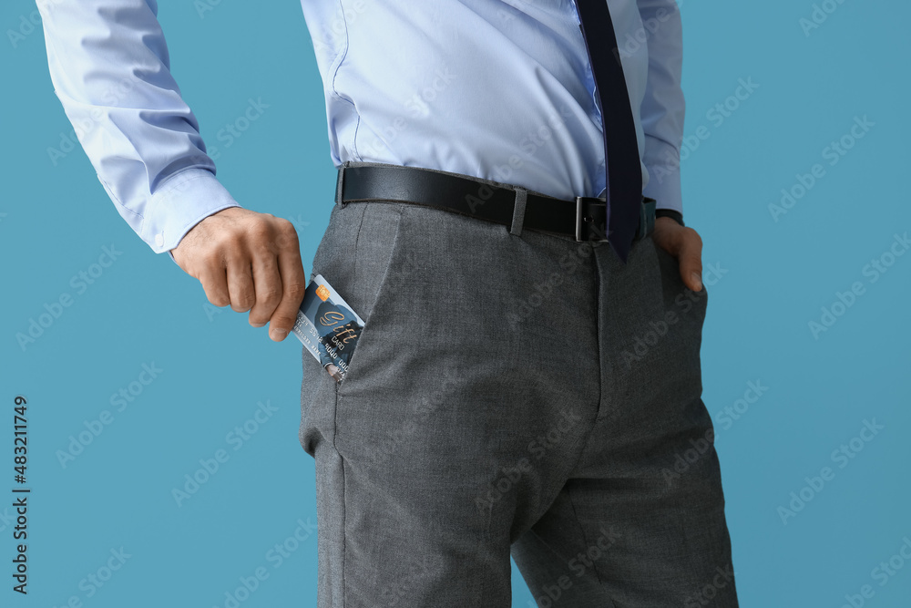 Handsome man in formal clothes putting gift card into pocket on color background, closeup