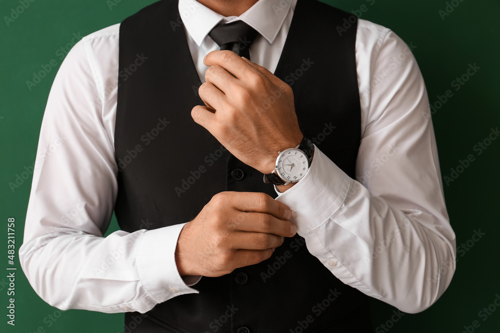 Gentleman in stylish formal clothes adjusting sleeve on color background, closeup