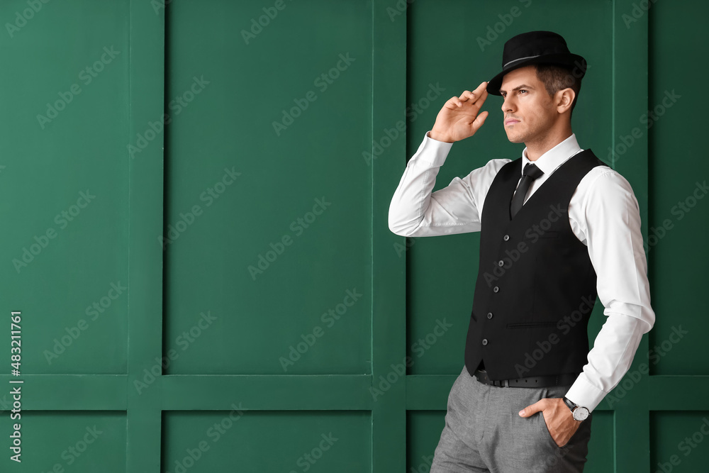 Gentleman in formal clothes wearing stylish hat on color background