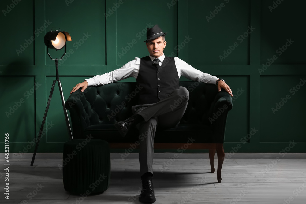 Gentleman in formal clothes and stylish hat sitting on sofa in dark room