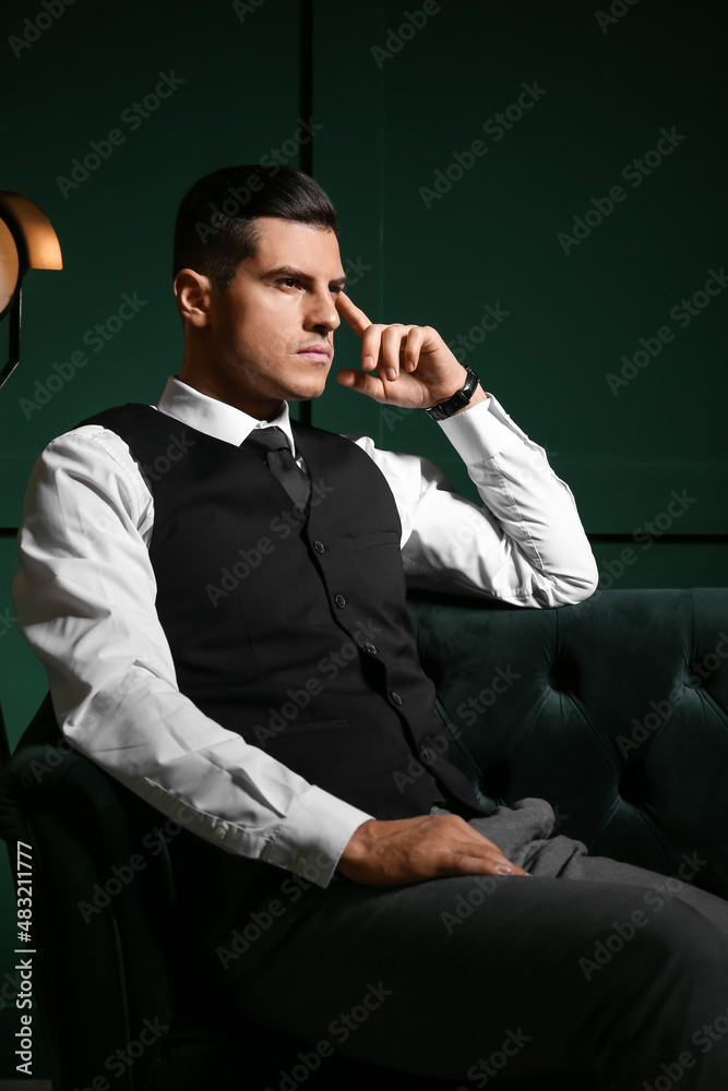 Pensive gentleman sitting on sofa in dark room