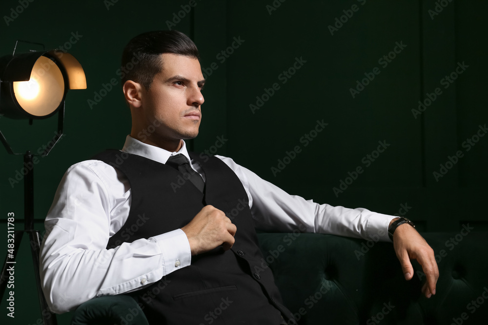 Fashionable gentleman sitting on sofa in dark room