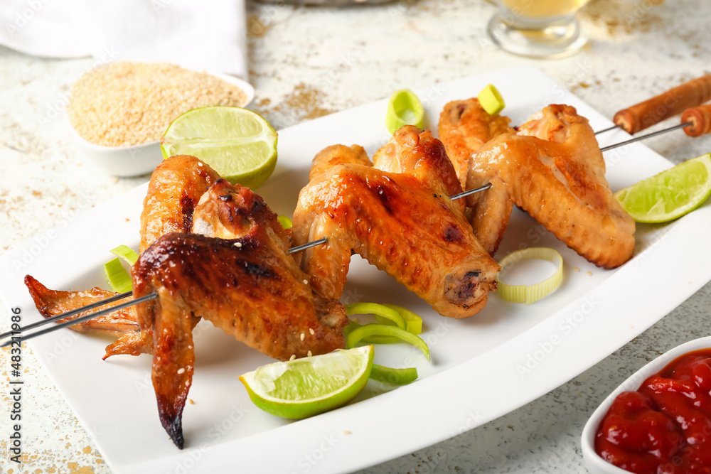 Plate with grilled chicken wings skewers and lemon on table