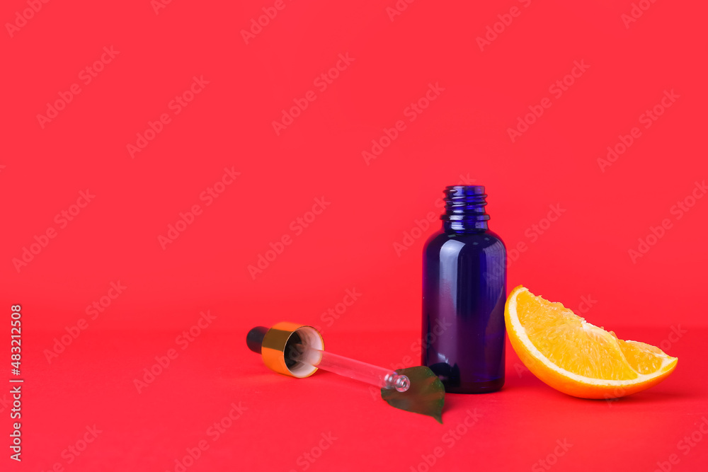 Bottle of essential oil and fresh cut orange on red background