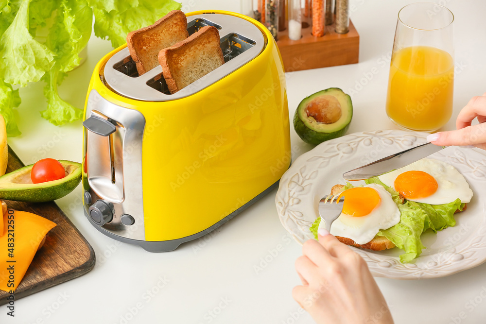 Woman having breakfast and yellow toaster with bread slices on white table