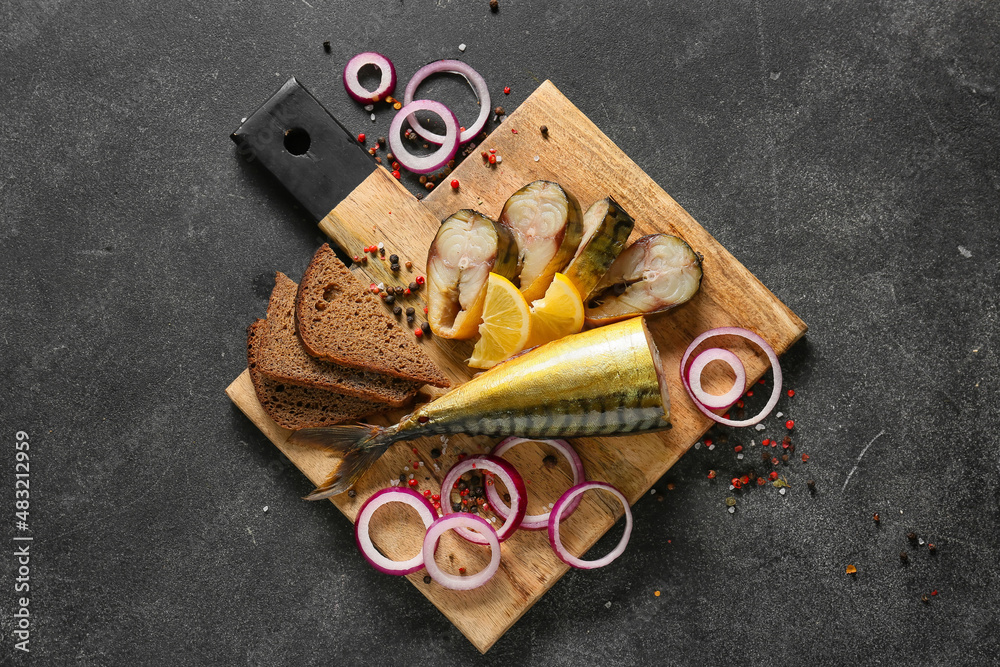 Wooden board with cut smoked mackerel fish and bread on black background