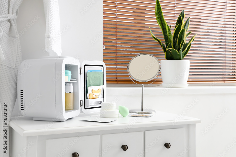 Small cosmetic refrigerator and mirror on dressing table near light wall