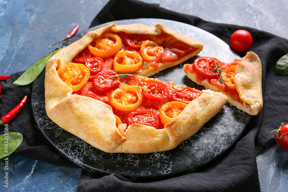 Plate with tasty tomato galette on blue background, closeup