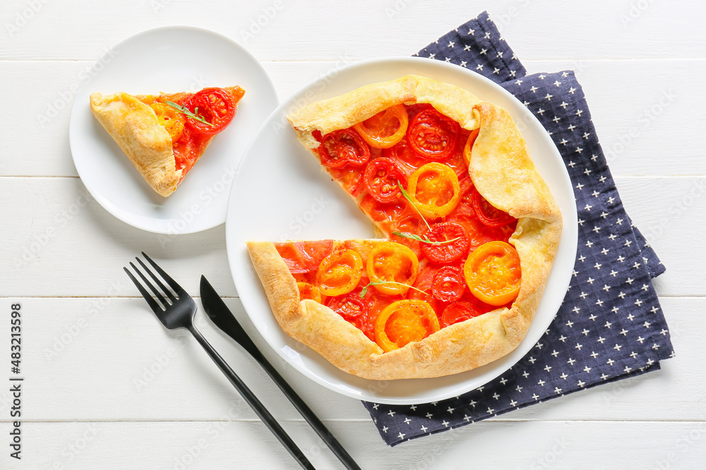 Plate with piece of tasty tomato galette on light wooden background