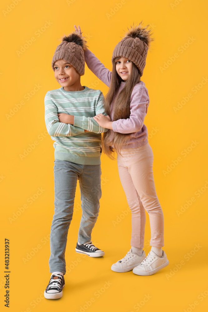 Funny little children in winter clothes on color background