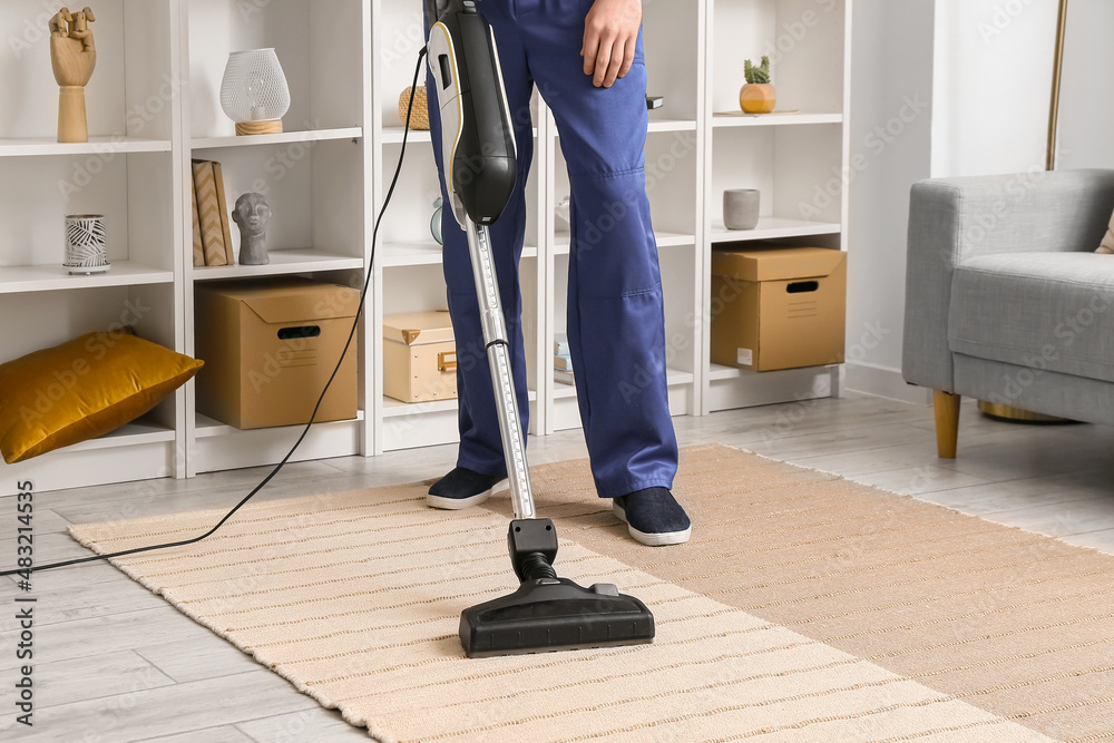 Male worker cleaning stylish carpet in room