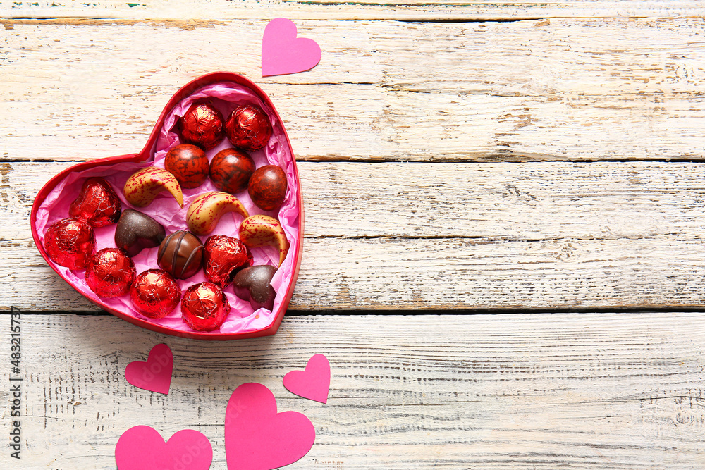 Heart shaped box with tasty chocolate candies on white wooden background