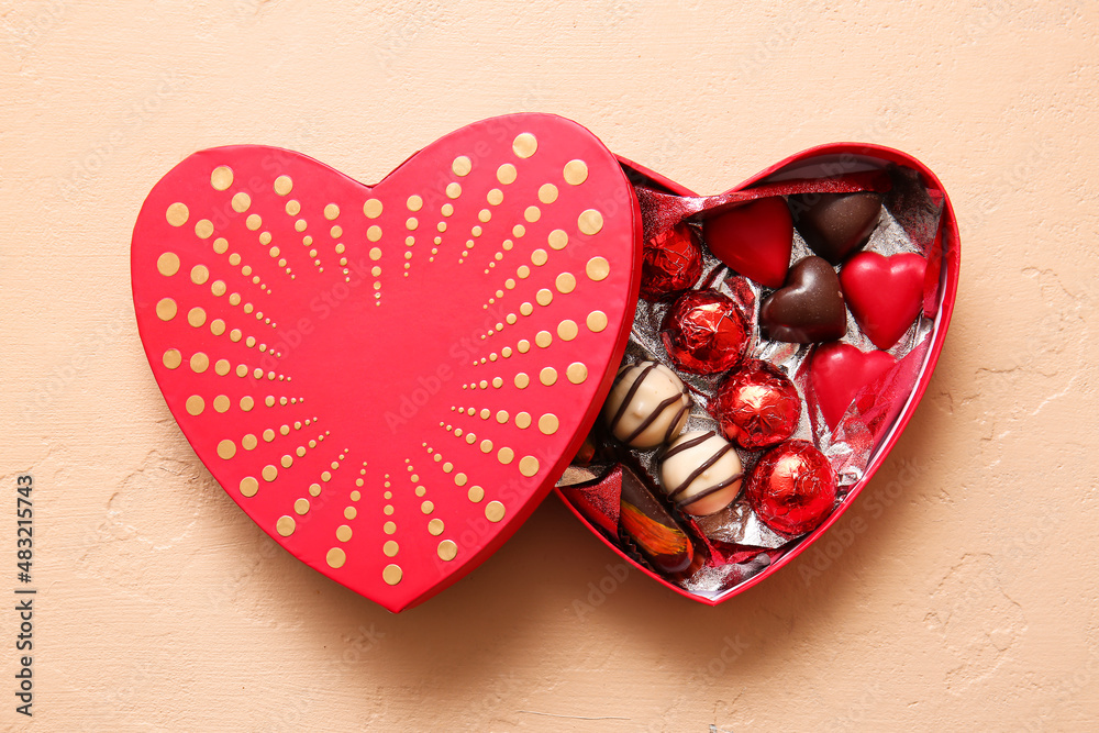 Heart shaped box with tasty chocolate candies on beige background