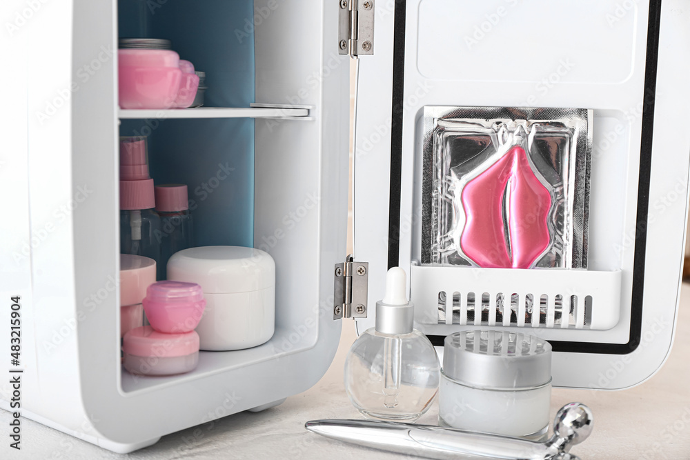 Small refrigerator with cosmetic products on table, closeup