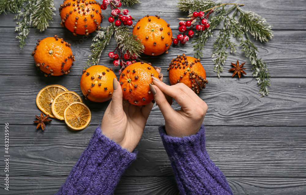 Woman making handmade Christmas decoration made of tangerine with cloves on dark wooden background