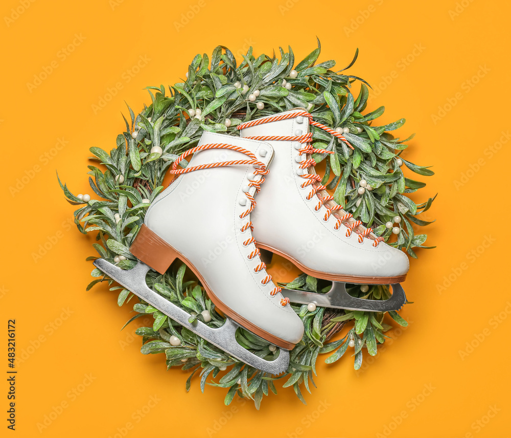 Ice skates and mistletoe wreath on orange background