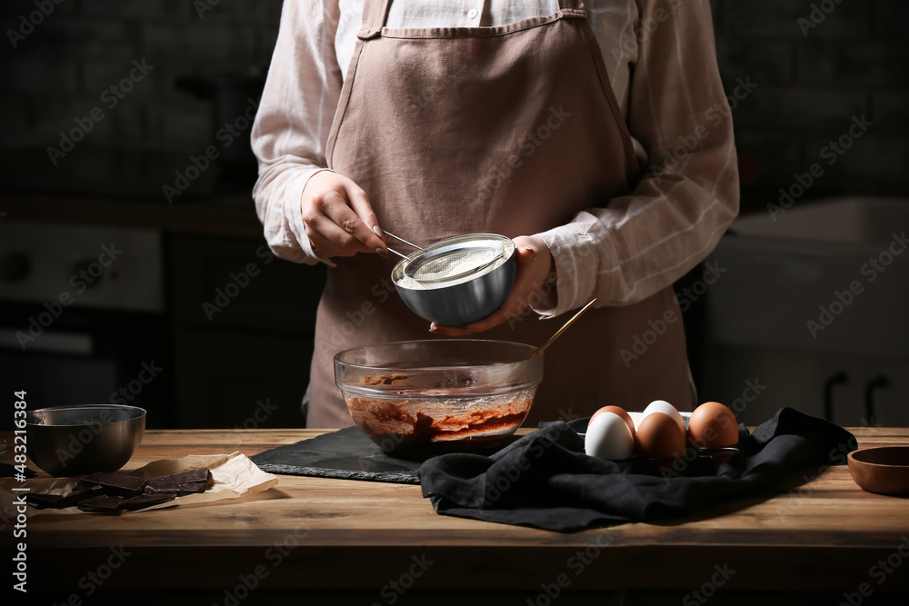 Woman adding flour for preparing chocolate brownie at kitchen table, closeup