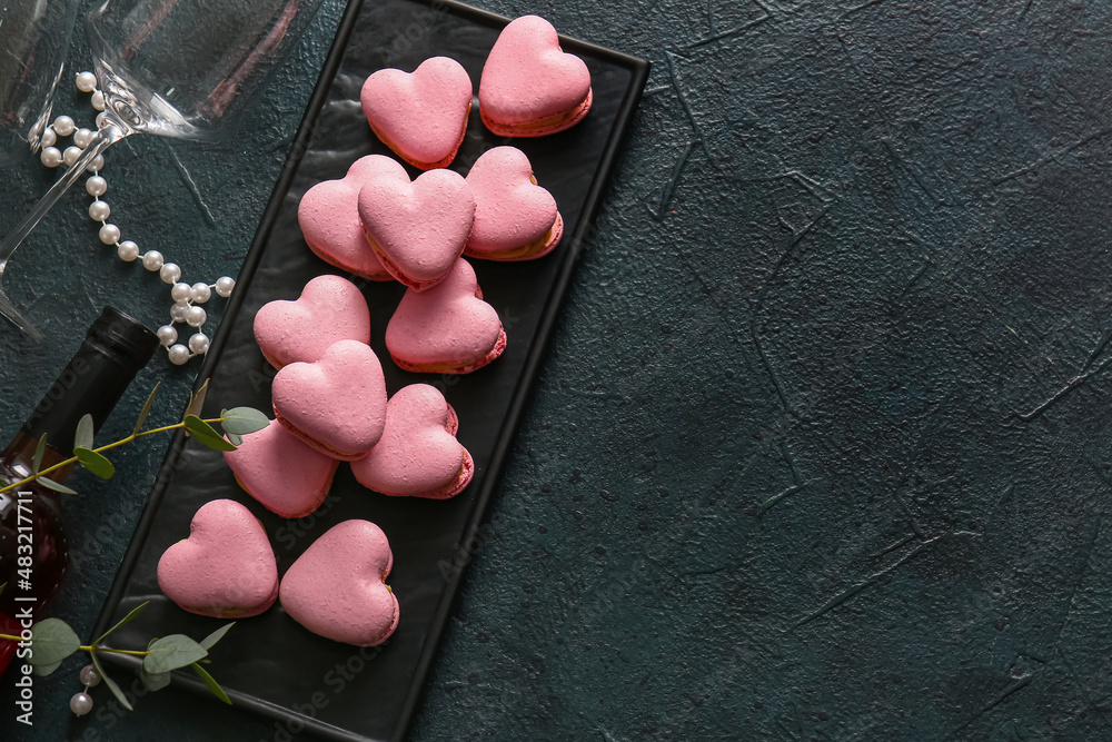 Board with tasty heart-shaped macaroons on black background