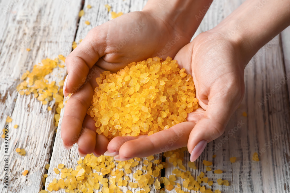 Female hands with orange sea salt on light wooden background, closeup