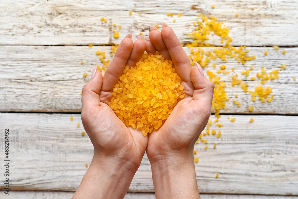 Female hands with orange sea salt on light wooden background, closeup