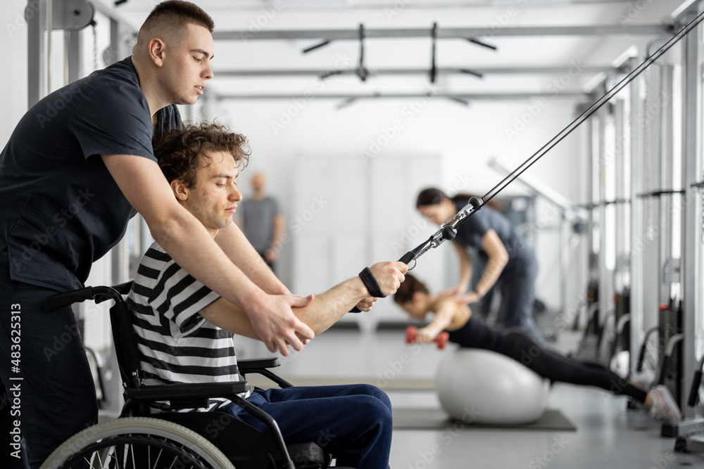 Rehabilitation specialist helps a guy in a wheelchair to do exercise on decompression simulator for 