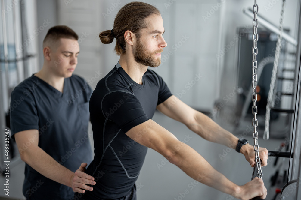 Man doing exercises on decompression simulators with the help of rehabilitation specialist. Concept 